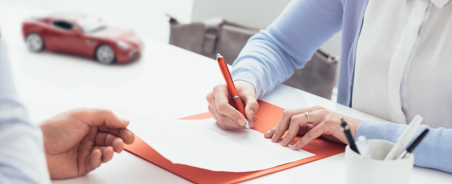 Woman signing a car insurance policy, the agent is holding the document